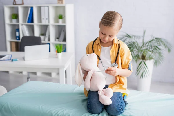 Kid holding toy and looking at electronic thermometer in hospital — Stock Photo