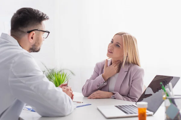 Woman touching sore throat during consultation with doctor near laptop — Stock Photo