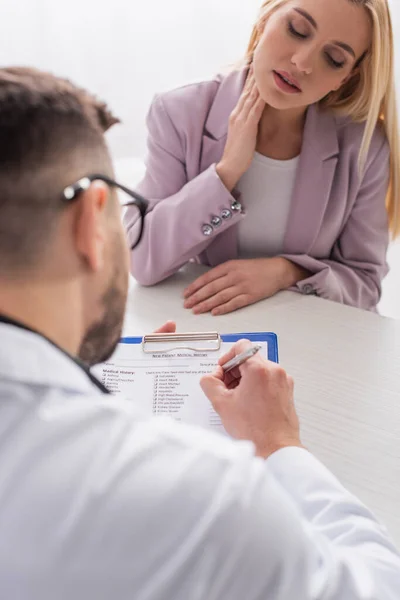 Verschwommener Arzt schreibt Rezept nahe blonder Frau im Krankenhaus — Stockfoto