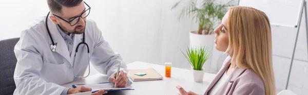 Doctor in eyeglasses writing on clipboard near blonde woman, banner — Stock Photo