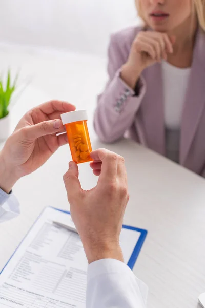 Cropped view of physician holding container with pills near blurred patient — Stock Photo