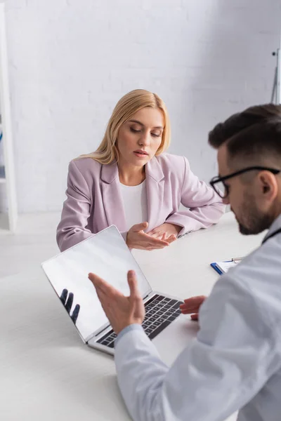 Femme et médecin pointant vers un ordinateur portable avec écran vierge pendant le rendez-vous à la clinique — Photo de stock