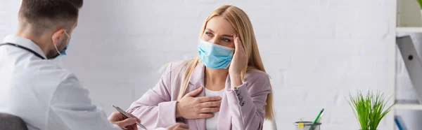Donna malata in maschera medica toccare testa e petto vicino medico offuscata, banner — Foto stock