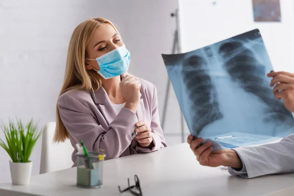 Mujer preocupada en máscara médica mirando los pulmones rayos X en las manos del médico en la clínica - foto de stock