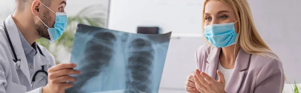 Médico en máscara protectora que muestra fluorografía a la mujer feliz en máscara médica, bandera - foto de stock