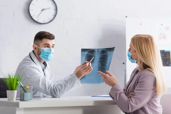 Médico y paciente en máscaras médicas que apuntan a la fluorografía durante la consulta en la clínica - foto de stock