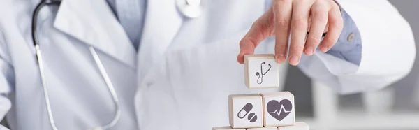 Vue partielle du médecin faisant pyramide de cubes avec icônes médicales, bannière — Photo de stock