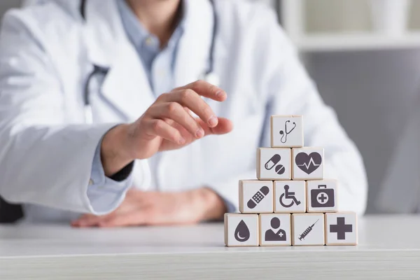 Піраміда кубиків з медичними ознаками біля розмитого лікаря в білому пальто, обрізаний вид — стокове фото