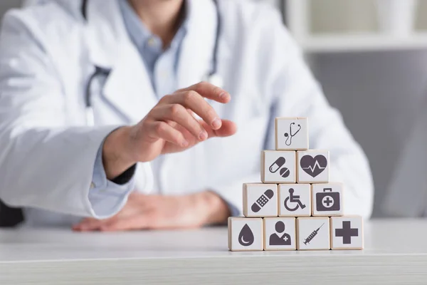 Piramide di cubi con segni medici vicino medico sfocato in cappotto bianco, vista ritagliata — Foto stock
