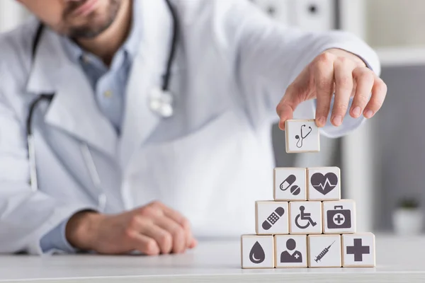 Vista parziale del medico sfocato che organizza cubi con simboli medici nella piramide — Foto stock