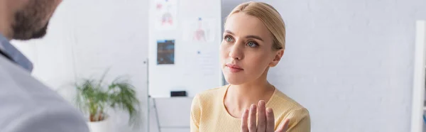 Mujer rubia hablando con médico borroso en el hospital, pancarta - foto de stock