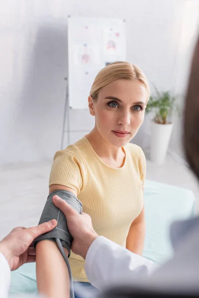 Rubia mujer mirando borrosa doctor poner manguito de tonómetro en su brazo - foto de stock