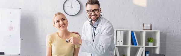 Счастливый врач и пациент смотрит в камеру во время диагностики в клинике, баннер — стоковое фото