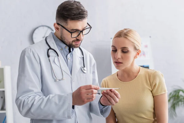 Donna bionda che guarda il termometro in mano al medico — Foto stock