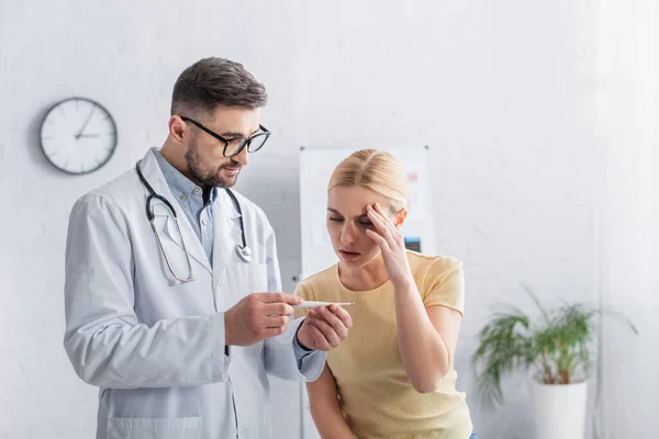 Médecin montrant thermomètre à la femme souffrant de maux de tête — Photo de stock