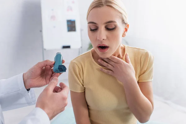 Doctor holding inhaler near woman touching throat while suffering from asthma — Stock Photo