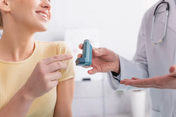 Visão cortada da mulher asmática sorrindo perto do médico apontando para o inalador — Fotografia de Stock