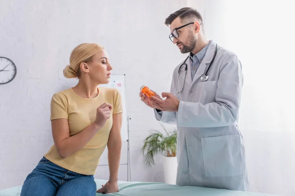 Physician in white coat showing pills to woman sitting on medical couch — Stock Photo