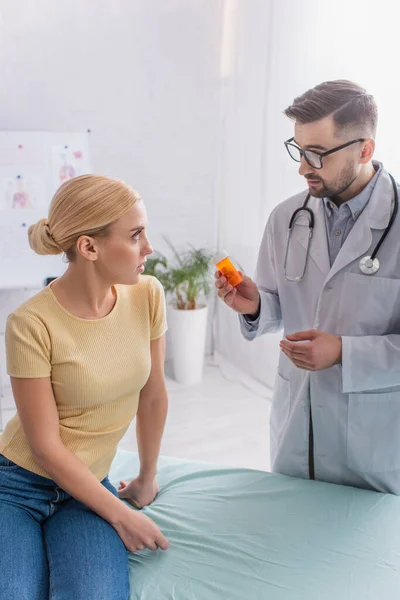 Médico mostrando medicamentos a la mujer rubia en el sofá médico - foto de stock