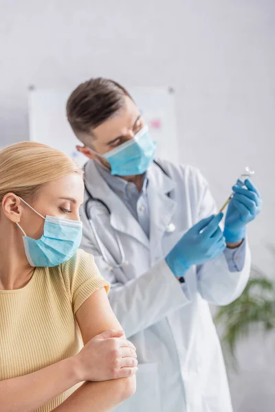 Mujer con máscara médica cerca del médico llenando la jeringa con la vacuna - foto de stock