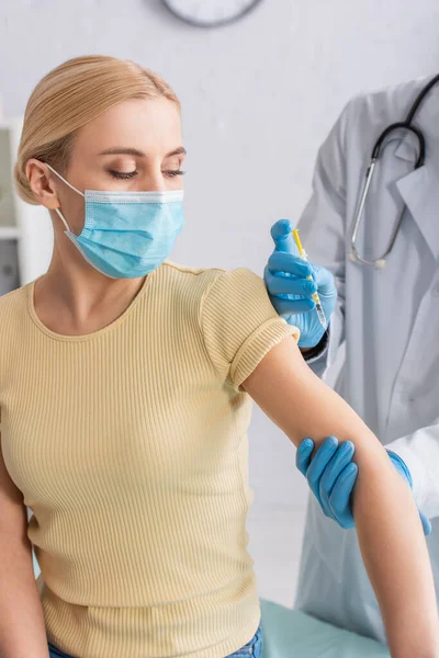 Médico en guantes de látex vacunar a la mujer en máscara médica en el hospital - foto de stock
