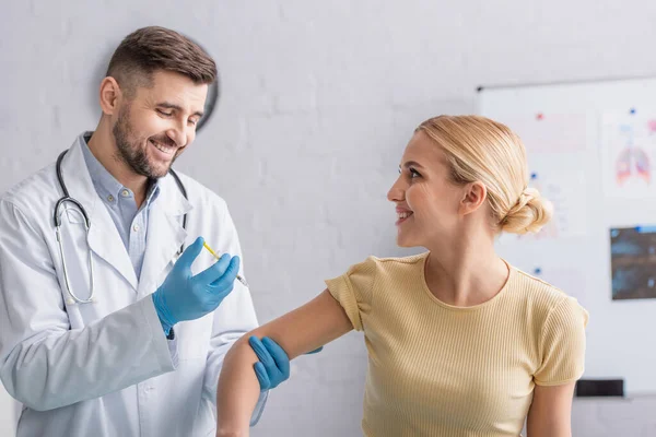 Положительный врач в латексных перчатках вакцинирует счастливую женщину в клинике — стоковое фото