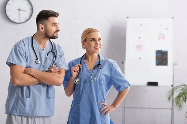 Médicos con uniforme azul y estetoscopios mirando hacia otro lado en el hospital - foto de stock