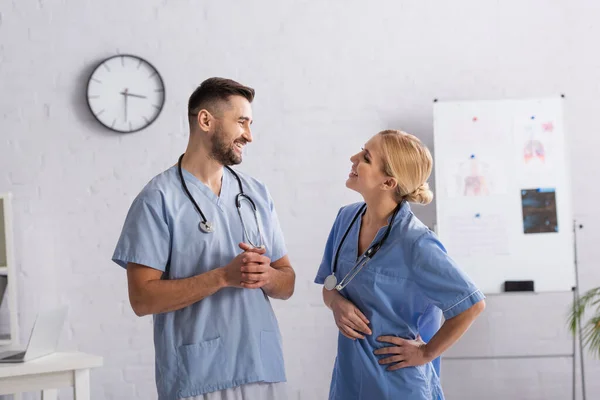 Медсестра стоїть з рукою на стегні, розмовляючи зі усміхненим лікарем — стокове фото