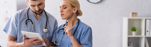 Médicos sérios em uniforme azul olhando para tablet digital no hospital, banner — Fotografia de Stock