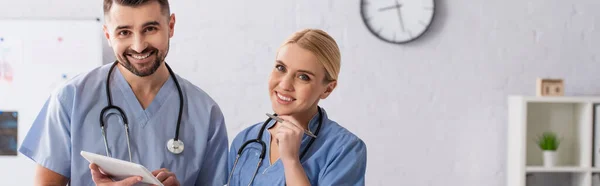 Médecins joyeux en uniforme bleu regardant la caméra à l'hôpital, bannière — Photo de stock