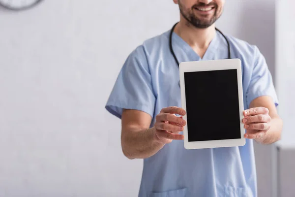 Vue recadrée du médecin souriant en uniforme bleu tenant tablette numérique avec écran blanc — Photo de stock