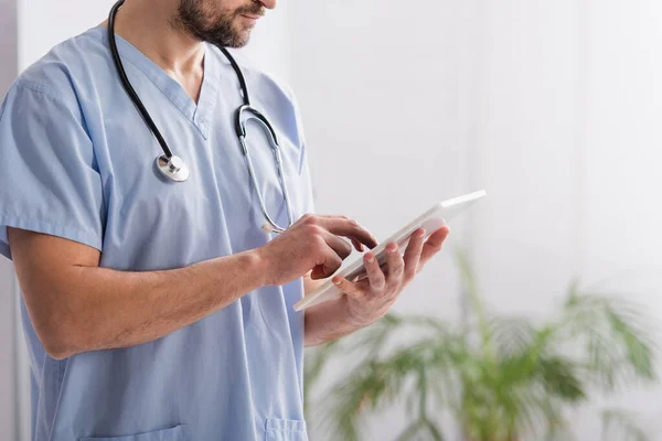 Vista parcial del médico en uniforme azul usando tableta digital en el hospital - foto de stock