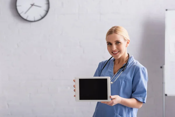 Médecin souriant en uniforme bleu montrant tablette numérique avec écran blanc — Photo de stock