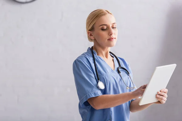 Врач в синей форме и стетоскоп на шее с помощью цифрового планшета в больнице — стоковое фото