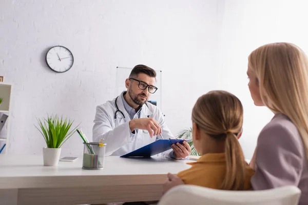 Pédiatre pointant vers le diagnostic tout en regardant la femme avec enfant à la clinique — Photo de stock