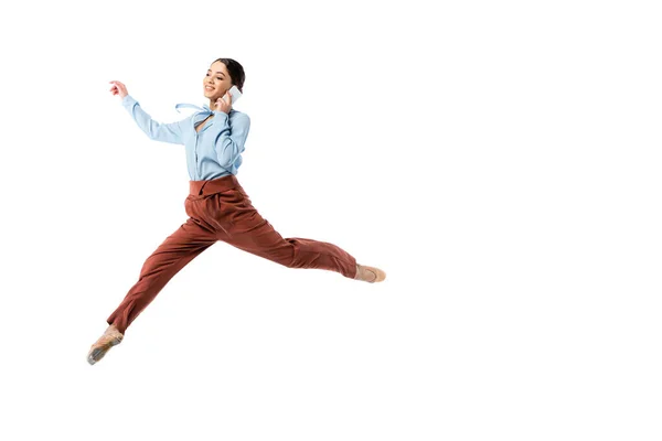 Smiling ballerina talking on smartphone while jumping isolated on white — Stock Photo