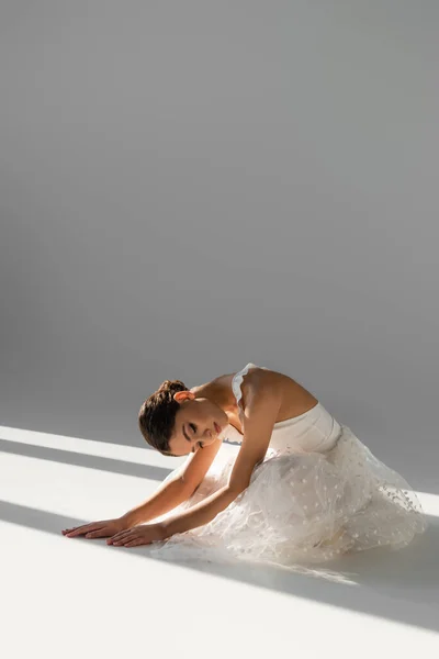 Балерина с закрытыми глазами сидит на сером фоне — стоковое фото