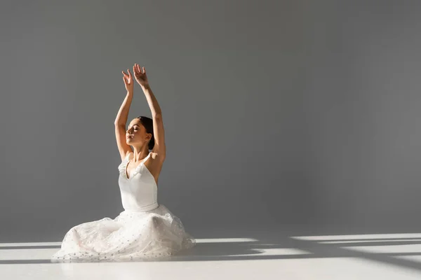 Ballerina mit geschlossenen Augen, die die Hände auf grauem Hintergrund hebt — Stockfoto