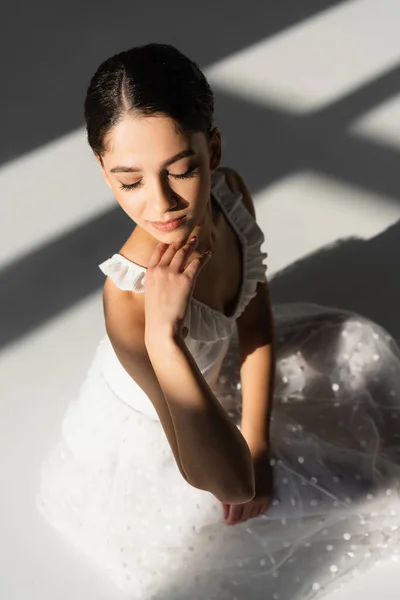 Vista de ángulo alto de la joven bailarina con los ojos cerrados sobre fondo gris - foto de stock