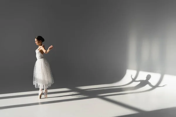 Вид сбоку брюнетки, танцующей на сером фоне с тенью — стоковое фото