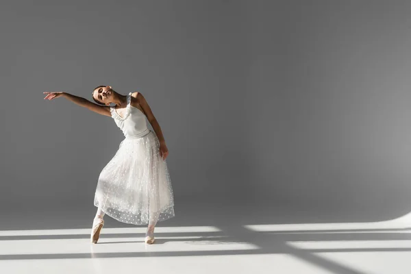 Ballerina tanzt mit geschlossenen Augen auf grauem Hintergrund mit Sonnenlicht — Stockfoto