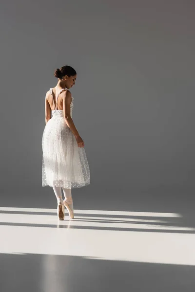 Side view of ballerina in white dress dancing on grey background — Stock Photo