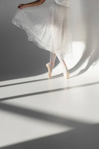 Vue recadrée de la ballerine en jupe blanche dansant sur fond gris — Photo de stock