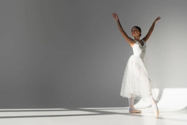 Young ballerina in white dress dancing on grey background — Stock Photo