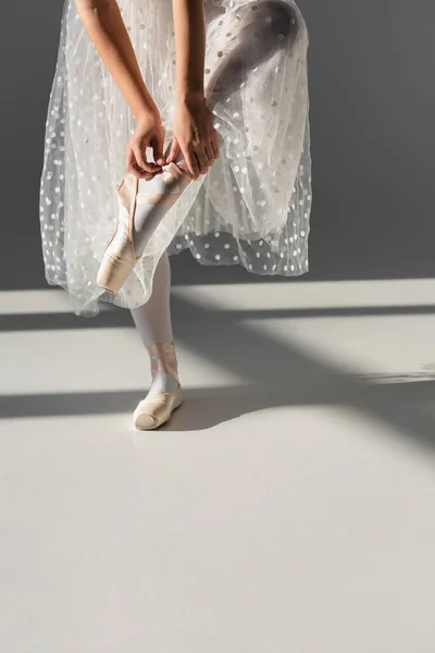 Cropped view of ballerina wearing pointe shoe on grey background with shadow — Stock Photo