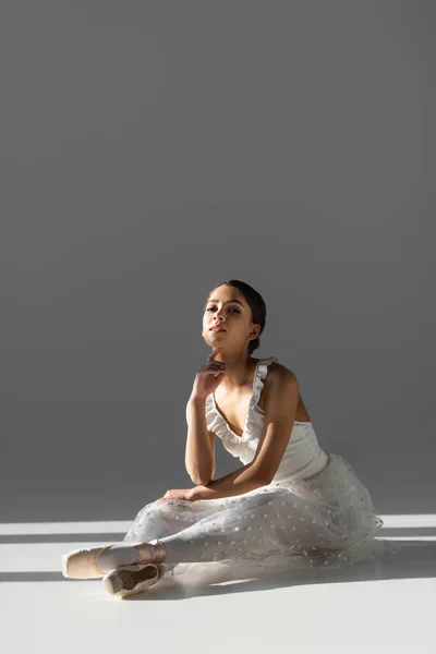 Brunette ballerine regardant la caméra sur fond gris avec la lumière du soleil — Photo de stock