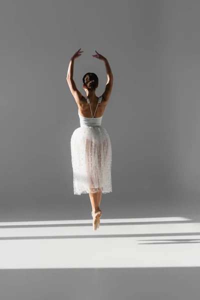 Vista trasera de bailarina bailando sobre fondo gris con sombra - foto de stock