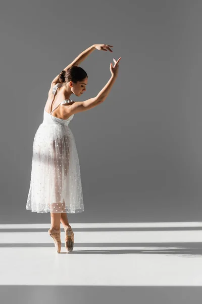 Vista laterale della ballerina che si piega e guarda in basso su sfondo grigio con luce solare — Foto stock