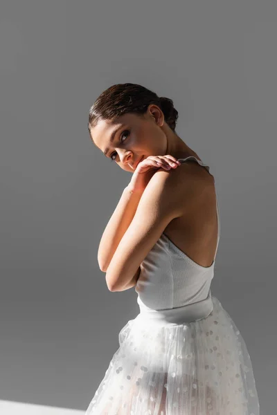 Pretty ballerina looking at camera on grey background with sunlight — Stock Photo