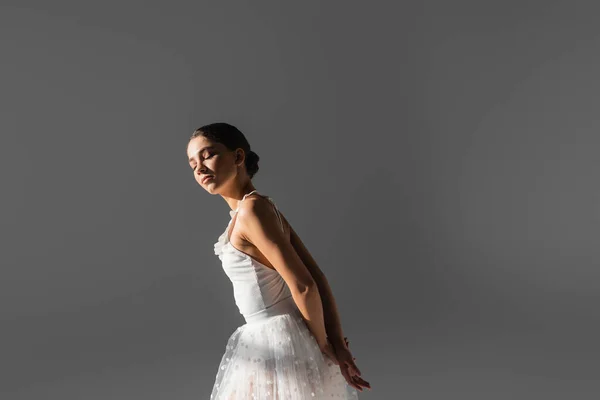 Young ballerina standing in sunlight isolated on grey — Stock Photo